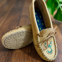 Load image into Gallery viewer, A pair of women's leather moccasins with a hand-beaded design, displayed alongside red roses on a wooden surface.