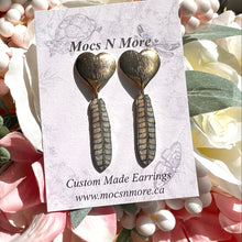 Load image into Gallery viewer, Heart-shaped earrings on a Mocs N More card with flowers in the background