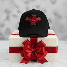 Load image into Gallery viewer, A black adjustable cap with a red embroidered eagle design on the front, displayed on a marble surface with roses and cookies in the background.