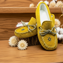 Load image into Gallery viewer, Yellow moccasins with decorative bows on a gray surface with flowers and lights.