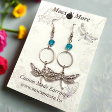 Load image into Gallery viewer, Dragonfly-themed earrings on a Mocs &#39;N More branded card against a black background
