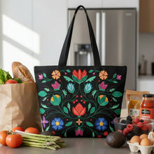 Load image into Gallery viewer, Black tote bag with colorful floral patterns on a reflective surface