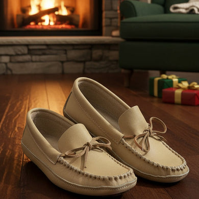 Pair of beige loafers on a wooden floor with a fireplace and green sofa in the background.