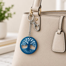 Load image into Gallery viewer, A handmade keychain featuring a circular blue glitter tree of life charm with white cutout details, attached to a silver clasp and a brown kraft paper card that reads 'Handmade with love'.