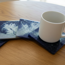 Load image into Gallery viewer, White mug on a set of blue coasters with white designs on a wooden table.