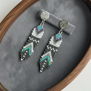 Pair of beaded earrings on a gray cushion inside a wooden frame.