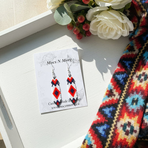 Pair of beaded earrings on a 'Mocs N More' card against a wooden background
