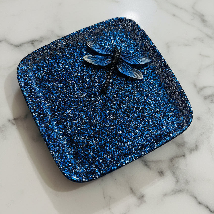 Blue glittery square object with a dragonfly on a beige surface