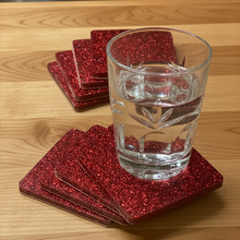 Load image into Gallery viewer, Clear glass of water on red glittery coasters on a wooden surface