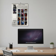 Load image into Gallery viewer, Spiral-bound 2027 calendar with artistic designs on a gray surface