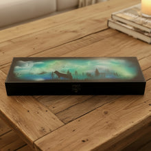 Load image into Gallery viewer, artwork on a box of a landscape with trees and a moonlit sky on a workbench.
