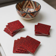 Load image into Gallery viewer, Red glittery coasters on a white surface with a patterned bowl in the background.