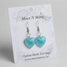 Load image into Gallery viewer, Turquoise heart-shaped earrings on a Mocs N More branded card with decorative background