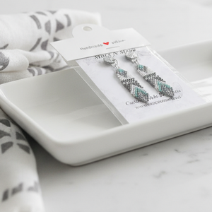 Earrings on a card with a white dish and patterned fabric on a marble surface