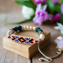 Load image into Gallery viewer, Beaded bracelet on a wooden block with flowers in the background
