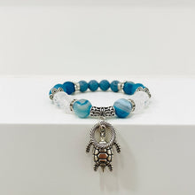 Load image into Gallery viewer, Bracelet with blue and white beads and a turtle charm on a wooden table.