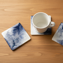 Load image into Gallery viewer, White mug on a wooden table with decorative coasters featuring blue abstract designs.
