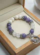 Load image into Gallery viewer, Purple and white beaded bracelet with a silver charm on a wooden box.