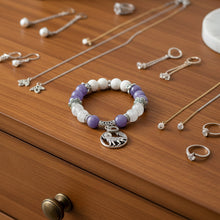 Load image into Gallery viewer, Bracelet with purple and white beads and a silver charm on a light gray background