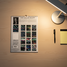 Load image into Gallery viewer, Back of calendar on desk with lamp and pen