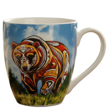 Load image into Gallery viewer, A white ceramic coffee mug featuring a colorful graphic illustration of a bear in traditional Indigenous-style patterns against a blue sky and grass background.