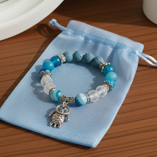 Load image into Gallery viewer, Blue beaded bracelet with a turtle charm on a blue drawstring bag on a wooden surface.